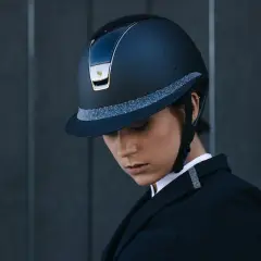 Elegancki kask marki kask, ozdobiony brokatową taśmą, noszony przez kobietę w czarnym żakiecie.