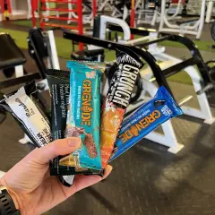 Une main tient plusieurs barres protéinées, parfaites comme collation avant ou après le sport, dans une salle de sport.