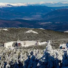 Edificio hotelero en la cabeza de Manzaneda, rodeado de pinos nevados y montañas al fondo.