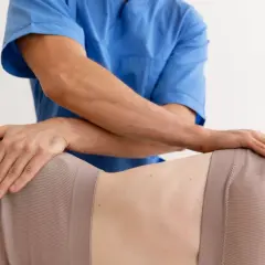 Fizjoterapeuta wykonuje masaż biodra, łagodząc mrowienie. Dłonie terapeuty obejmują okolicę biodrową pacjentki.