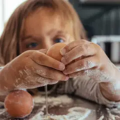 Kind mit bemehlten Händen knackt Eier. Vorsicht vor salmonellen eiern, besonders bei rohem Verzehr.