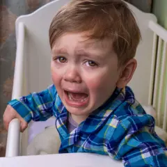Un niño pequeño con pijama a cuadros llora desconsoladamente en su cuna. Sus ojos están llenos de lágrimas y su boca abierta en un grito.
