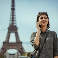 Uśmiechnięta kobieta rozmawia przez telefon w Paryżu, niedaleko Wieży Eiffla. Dowiedz się, jak uruchomić roaming w Play, by cieszyć się rozmowami za granicą.