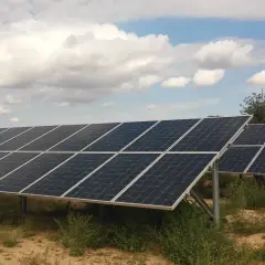 Rzędy paneli fotowoltaicznych na tle błękitnego nieba z chmurami. Firma oferuje sprzedaż energii z fotowoltaiki.