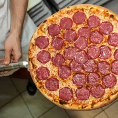 Pizza z salami na łopacie, trzymana przez kucharza.