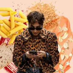 Frau im Leo-Mantel checkt ihr Handy, umgeben von Nudeln, Brot, Reis und Haferflocken. Sie fragt sich, wie viel Kohlenhydrate am Tag gesund sind.