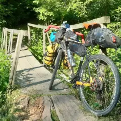 Rower wyprawowy na drewnianym moście, gotowy na mazowiecki gravel. Otoczony bujną zielenią, zaprasza do przygody.