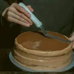 Ręce wygładzają czekoladowy krem maślany pod opłatek na torcie.