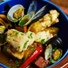 Delicioso bacalao con almejas y gambas, servido en un cuenco azul con perejil picado y un chile rojo.