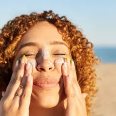 Frauenhände verteilen Sonnencreme mit Methylene bis-benzotriazolyl tetramethylbutylphenol auf der Nase.