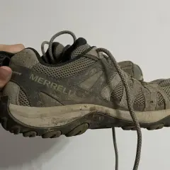 A muddy Merrell hiking shoe is held up, showing its worn tread. This image might inspire ideas on how to rough up the bottom of slippery shoes for better grip.