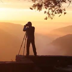 Fotograf na skale, wykonujący pomiar światła o wschodzie słońca. Mgła spowija doliny, tworząc malowniczy krajobraz.