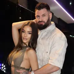 Wojtek Gola z dziewczyną, w eleganckich strojach, pozują do zdjęcia w nastrojowym wnętrzu.