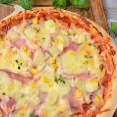 Apetyczna pizza z ananasem, szynką, kukurydzą i serem, ozdobiona świeżymi ziołami.