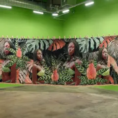 A tapestry at little April Galleries features four portraits of women amidst lush tropical foliage and pineapples.