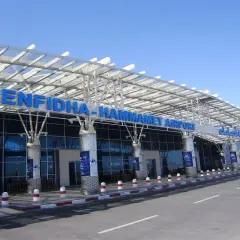Nowoczesny budynek lotniska Enfidha-Hammamet w Tunezji, z niebieskimi literami nazwy i szklaną fasadą.