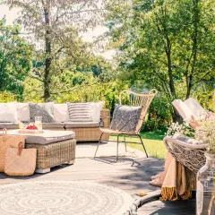 Relaks na tarasie w stylu boho: rattanowe meble, plecione kosze i okrągły dywan tworzą przytulną przestrzeń. Inspiracje dla Twojego ogrodu.
