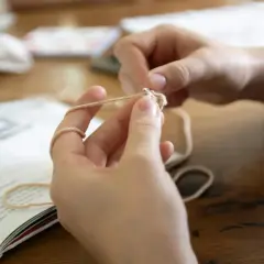 Mani che imparano il lavoro a maglia per principianti, seguendo un libro di istruzioni.