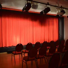 Rote Vorhänge und leere Stühle im **theas theater**. Scheinwerfer sind an der Decke montiert, bereit für die nächste Vorstellung.