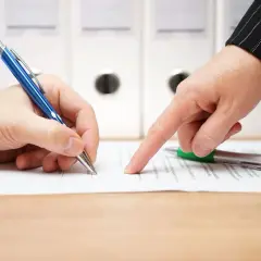 Dwie osoby przy biurku omawiają umowę. Jedna podpisuje dokument, druga wskazuje palcem na tekst. To ważny moment dla zleceniobiorców.