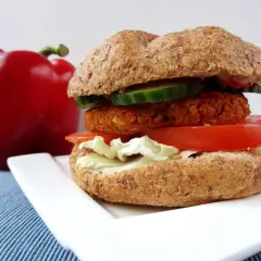 Pyszny burger z ciecierzycy z pomidorem, sałatą i ogórkiem, obok czerwona papryka.
