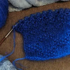 Un échantillon de tricot bleu vif, avec une pelote de laine assortie et une aiguille. La jauge maille est bien visible sur le tissu.
