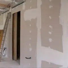 Scianka dzialowa z plyty kartonowo gipsowej w trakcie prac. Widoczne drabiny, instalacje i otwór drzwiowy.