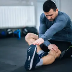 Mężczyzna wykonuje rozciąganie nóg na siłowni, siedząc na macie.