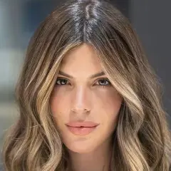 Mujer con pelo castaño con canas y mechas rubias, con ondas suaves y raya en medio.