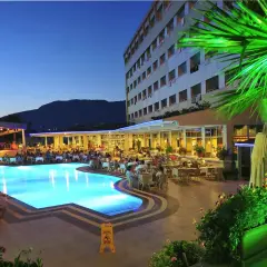 Wieczorny relaks przy basenie w Kirbiyik Resort Hotel. Goście siedzą przy stolikach, a basen lśni błękitem.
