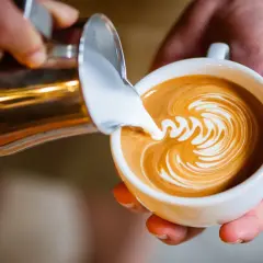 Barista tworzy latte art, wlewając spienione mleko do kawy. Idealne mleko do cappuccino to podstawa pięknego wzoru.