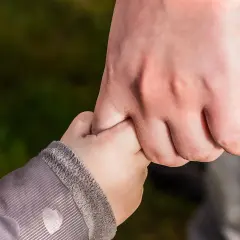 Dłoń dorosłego trzyma dłoń dziecka. Symbol wsparcia i bezpieczeństwa, jak w przypadku przedawnienia spadku po rodzicach.
