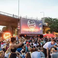 Stor publik samlad för utomhusbio under Stockholms Filmfestival. En stor duk visar festivalens logotyp.