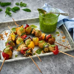 Grillade vegetariska grillspett med potatis, paprika och zucchini, serverade med en grön sås.
