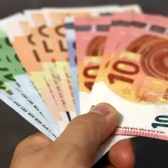 Main d'une personne tenant plusieurs billets en euros, dont des 10€ et 100€. Une scène évoquant une reclamation caisse epargne.
