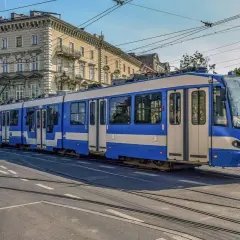 Niebiesko-biały tramwaj na torach w Krakowie. To część krakowskiej komunikacji miejskiej, która przewozi pasażerów przez miasto.