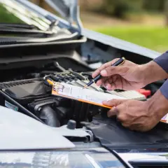 Un meccanico controlla il motore dell'auto con una penna e una cartella, chiedendosi: "quanto tempo ho per fare la revisione?".