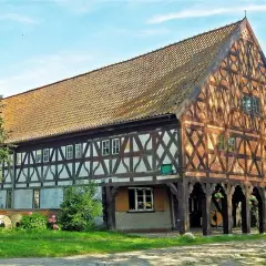 Drewniany dom podcieniowy, część szlaku mennonitów, z charakterystyczną kratownicą i ceramicznym dachem.
