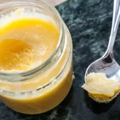 En burk med gyllene ghee och en sked med lite av det. Perfekt för ditt ghee recept!
