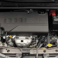 Silnik Toyoty Yaris, widok z góry. Czarna osłona z logo Toyoty, akumulator Varta, płyny i przewody.