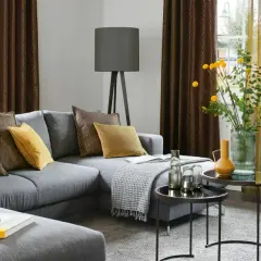 Gemütliches Wohnzimmer mit grauem Sofa, Kissen in Braun und Gelb, sowie moderne Fenstergestaltung mit zweifarbigen Vorhängen.