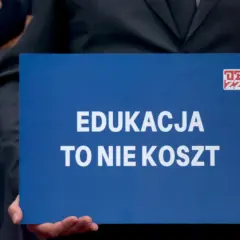Niebieska tablica z białym napisem "EDUKACJA TO NIE KOSZT" i logo ZZ.