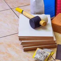 Outils pour coller du carrelage avec du ciment : carreaux, maillet, truelle, éponges, brosse, croisillons et sacs de ciment.
