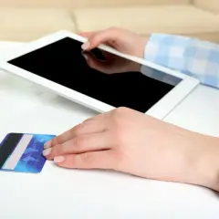 Dłonie trzymają tablet i kartę płatniczą. Zastanawiasz się, jak aktywować BLIK w Millenium?