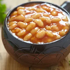 Un bol en terre cuite rempli de haricot blanc en sauce tomate, garni de persil frais sur fond de bois.