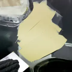 Ręka w czarnej rękawiczce rozprowadza szpachlę na karoserii, pokazując, jak szpachlować samochód.