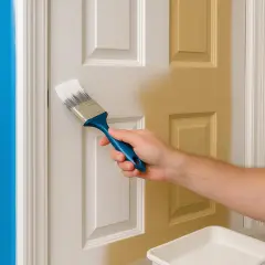Main tenant est en train de peindre une porte. La moitié de la porte est déjà peinte en jaune, l'autre moitié est blanche.