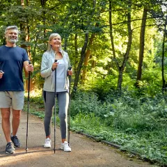 Älteres Paar genießt Nordic Walking im Wald. Eine gute Aktivität bei Bandscheibenvorfall zur Stärkung der Rückenmuskulatur.