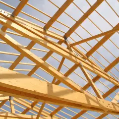 Structure en bois d'une charpente, vue de dessous. Le ciel bleu et nuageux est visible à travers les poutres. Un aperçu pour estimer le prix charpente.