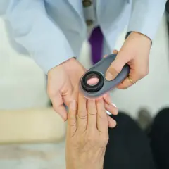 Lekarz w błękitnej **ropie** bada dłoń pacjenta dermatoskopem.